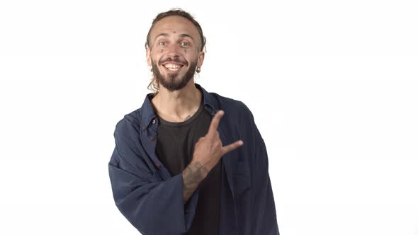 Cheerful Bearded Man with Tattoos on Body and Face Smiling Joyful Showing Rocknroll Gesture Standing