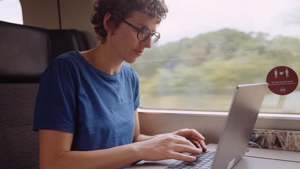 Woman in Glasses Working on a Laptop While Going By Train