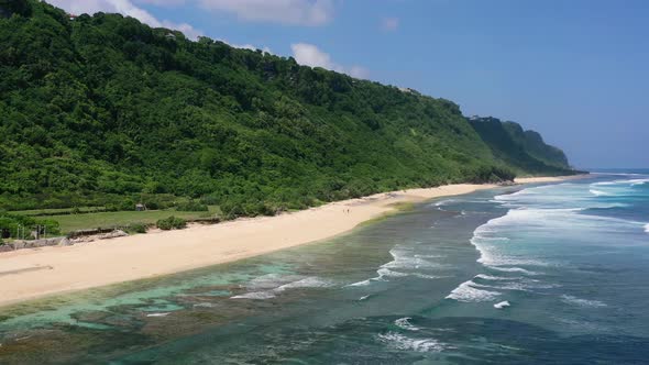 ocean waves crash on empty white sand Nyang Nyang Beach in Uluwatu Bali with large mountain cliffs,