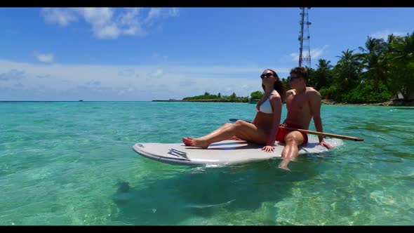 Man and lady sunbathing on idyllic coast beach trip by blue sea with white sandy background of the M