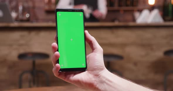 Man Holds a Modern Smartphone with Green Screen on