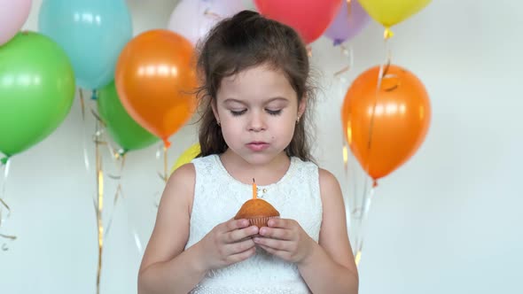 Pretty Girl in White Dress Blows Burning Candle on Cupcake