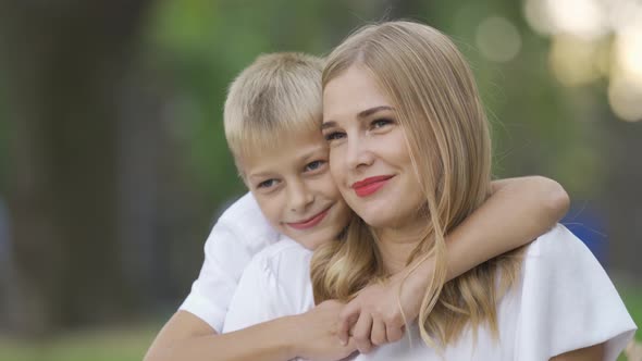 Portrait of Young Caucasian Woman and Little Boy Sitting in the Park or Forest