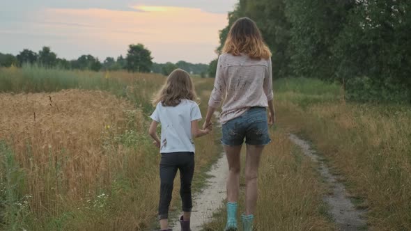 Two Happy Girls Sisters Walking After the Rain in Dirty Clothes Holding Hands Back View