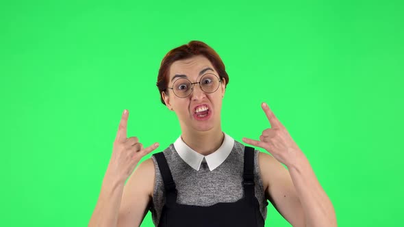 Portrait of Funny Girl in Round Glasses Is Making a Rock Gesture and Enjoying Life. Green Screen