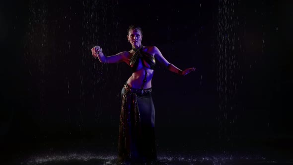 A Woman is in a Studio in the Pouring Rain on a Dark Background Making Beautiful Movements and