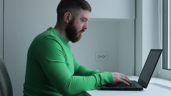 Close up view of bearded middle aged man in green t-shirt using laptop computer