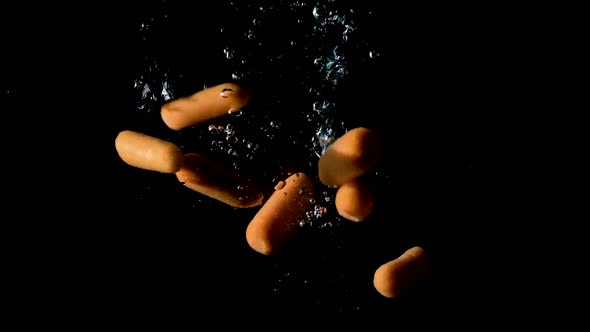 Baby carrots dropped into water on black background, slow motion close up
