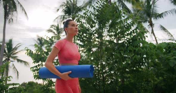 Woman Walks Up the Hill After Yoga Exercise She Dressed in Pink Sportswear and Carry a Blue Mat