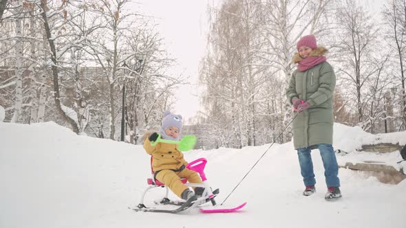 A happy mom rides a joyful toddler 15-23 months old on a snowcat sled