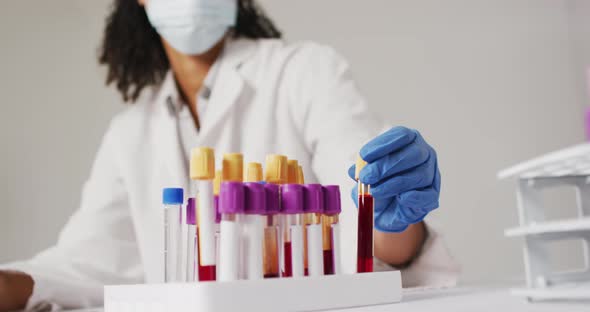 Video of biracial female doctor with face mask holding test tube on blue background