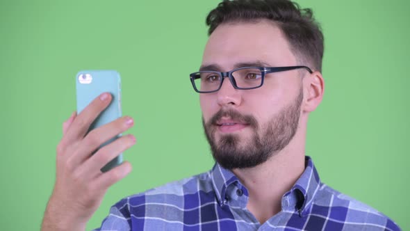 Face of Happy Young Bearded Hipster Man Using Phone