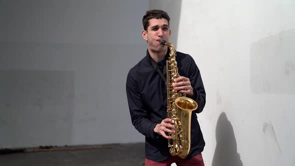 a Man in a Dark Shirt and Red Trousers Plays the Saxophone Emotionally Against a White Wall. the