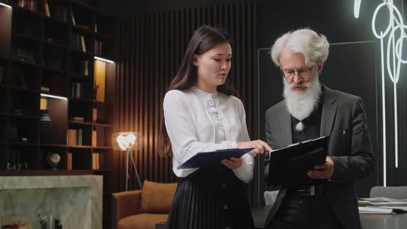 Young Asian Girl Talks with Elderly Colleague About Some Information in Office