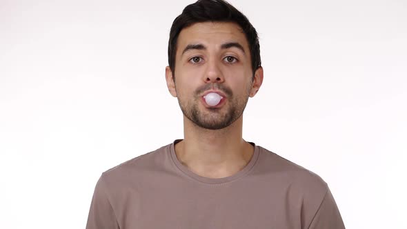 Front View of European Dark Haired Young Bristled Man Blowing Chewing Gum Bubble with Eyes Wide Open