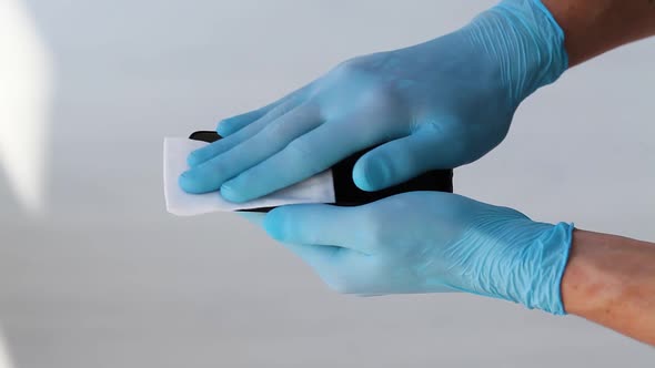 Men is hands in medical rubber gloves to rub a mobile phone.