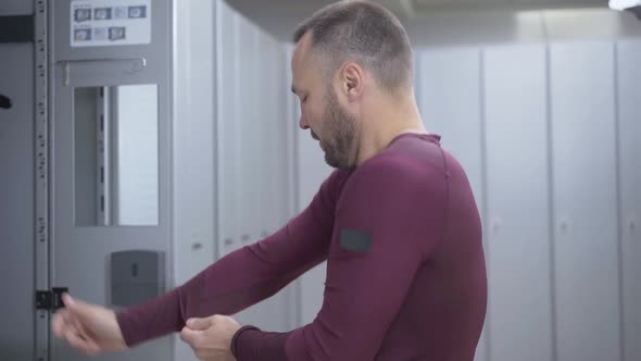 Side View of Confident Adult Sportsman Dressing Up in Gym Locker Room. Middle Shot of Bearded