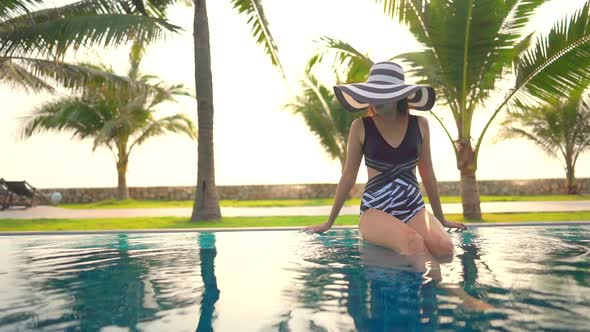 Sexy Asian Woman in Black and White Swimsuit and Sunglasses Resting on the Edge of an Exotic Resort