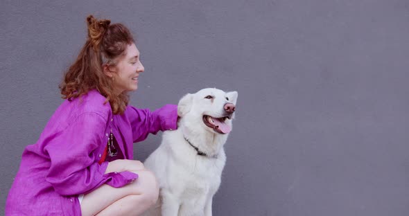 girl in pink shirt is petting a big white dog on the head and smiling