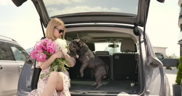 Young Woman with Bulldog and Flowers Sit in a Car Trunk