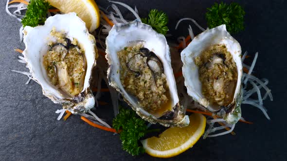 Cooked Oysters in Shell with Garlic and Lemon on Black Textured Slate Background