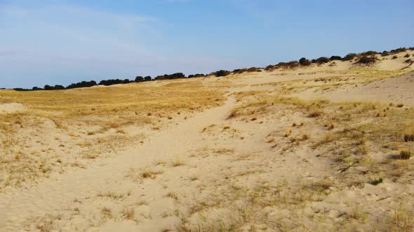 AERIAL: flying backwards over the sand dune and revealing clear blue sky