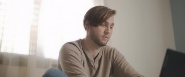 A close up of a young man sitting in bed and working on a computer. 