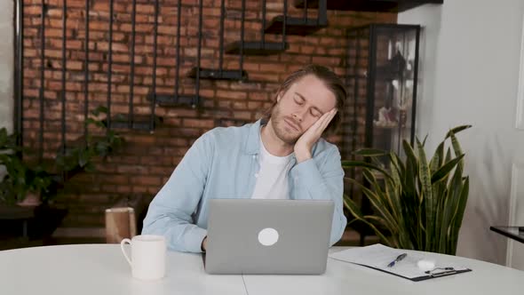 Freelancer Sitting at Work Desk Holding His Head with His Hands Tired of Working in Laptop Need Rest