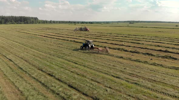 Picturesque Landscape with Several Tractors Mowing and Removing Fresh Grass for Animal Feed