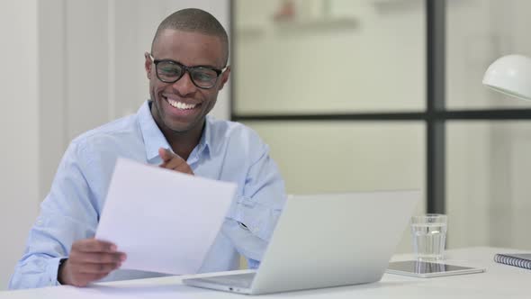 African Man Reading Documents Working Laptop