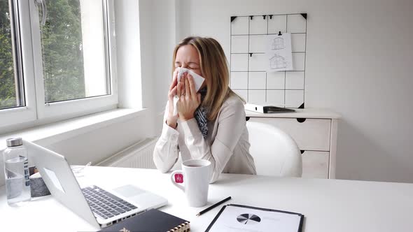 Sick businesswoman blowing nose while working in office