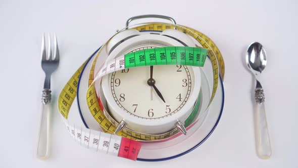 Alarm clock on a white plate with a blue border and a spoon with a fork on the table.