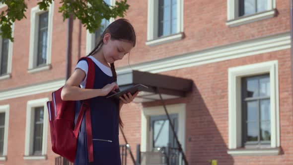 Happy Preteen Girl with Backpack and Tablet Pc Standing at Entrance to School