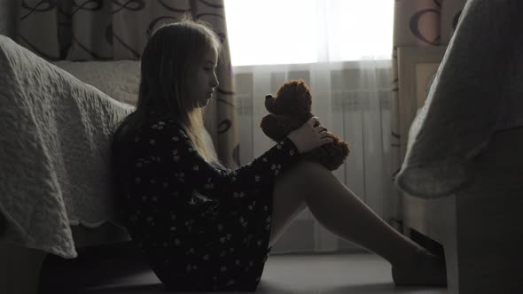 Depressed Little Girl and Her Best Friend Teddy Bear in the Dark Gloomy Room of His House