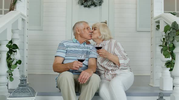 Attractive Senior Elderly Caucasian Couple Sitting and Drinking Wine in Porch at Home, Making a Kiss