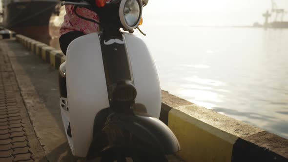 Young Beautiful Girl Speaking on Phone Near Sea on Scooter at Sunrise