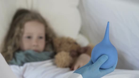 Little Frightened Girl Looking at Enema in Doctor's Hand