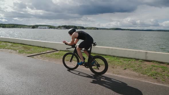 Triathlete Rides a Cutting Bike Pro Cyclist Rides on a Track Near a Lake Athlete Training for