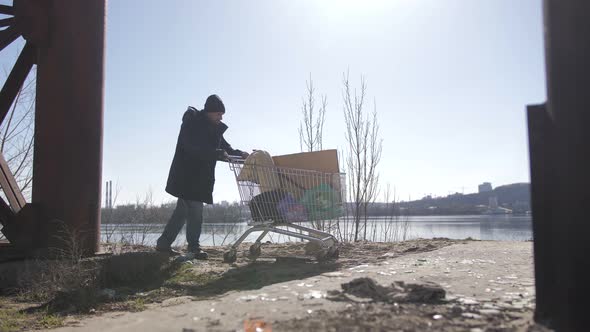 Homeless Male Walking Under Bridge with Cart