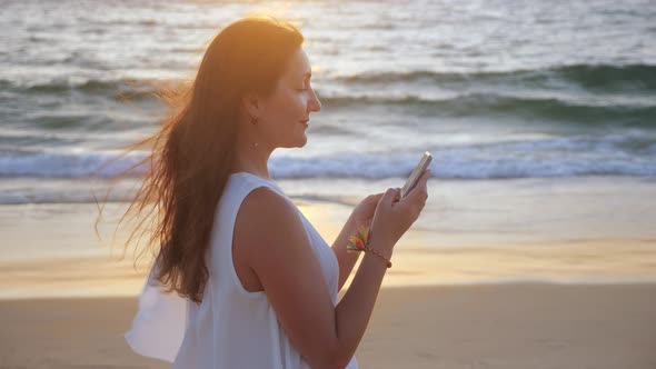 Girl Typing on Smartphone on Ocean Beach at Sunset