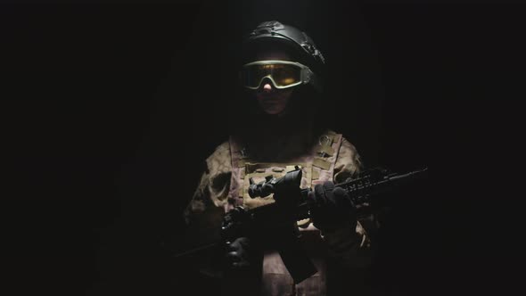 Woman in a Helmet Glasses and Military Uniform Holds a Rifle Standing in Dark of Studio