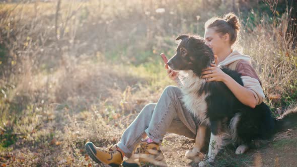 A Young Adult Woman Taking a Selfie with Her Dog While Sitting on a Hill