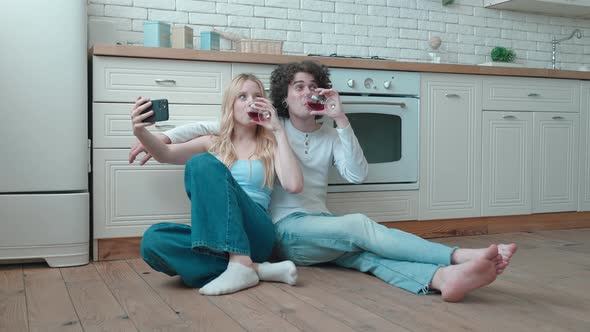 Loving Couple Happy Young Guy and Blonde Woman Taking Selfie Sit on Cozy Kitchen Room Floor Hold