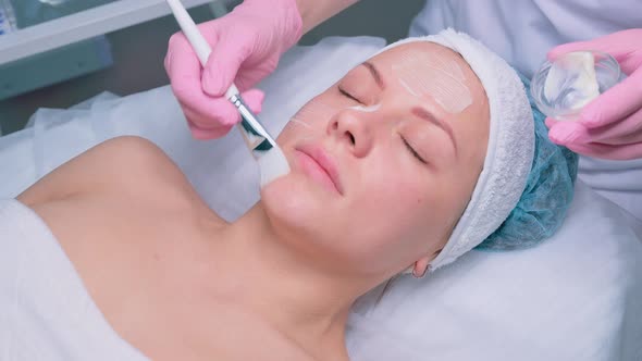 Cosmetologist Applying Face Moisturizing Mask on Young Woman's Face