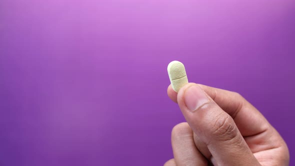 Hand Holding Pills on Purple Background with Copy Space 