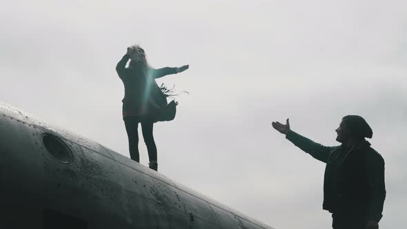 Young Woman Standing on the Top of Crashed DC-3 Plane in Iceland and Reaching Out the Hand To Man