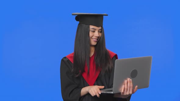 Portrait of Female Student in Graduation Costume Talking for Video Chat Using Laptop and Rejoice