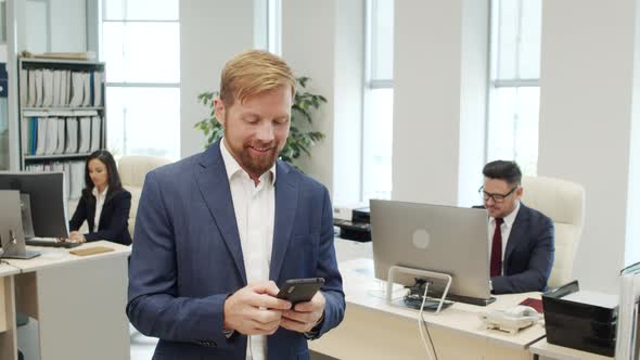 Cheerful Manager Texting on Mobile Phone in Office