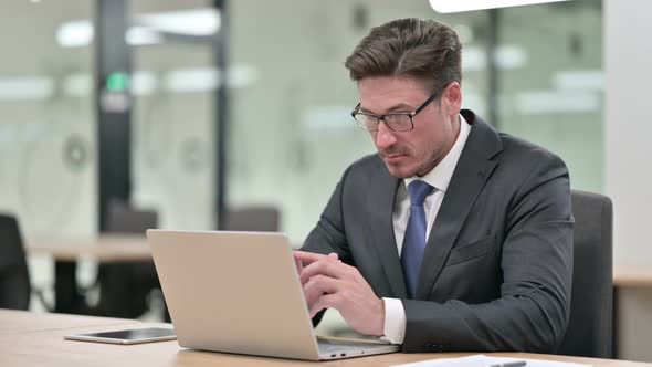 Pensive Middle Aged Businessman Thinking and Working on Laptop in Office