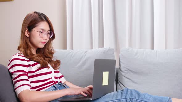 Young Asian woman sitting on sofa using a notebook to shop online.
